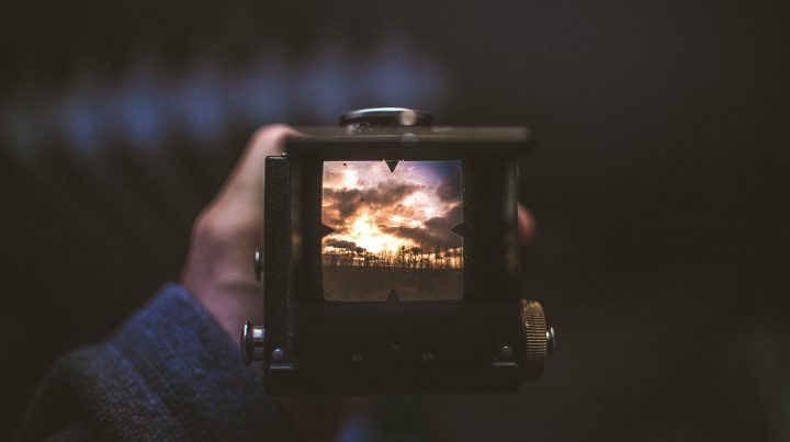 A man holding a camera looking through the viewfinder at a beautiful sunset